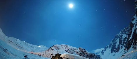 Paisaje montañoso cubierto de nieve bajo un cielo nocturno con una luna brillante.