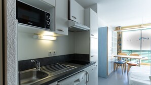 Una cocina compacta equipada con microondas, estufa y lavavajillas. Cuenta con un pequeño comedor con mesa y sillas.