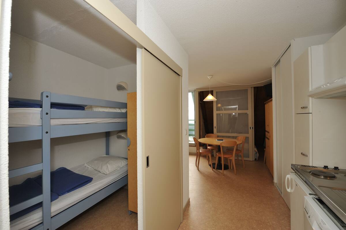 A compact room with bunk beds, a small dining table, and a kitchenette.