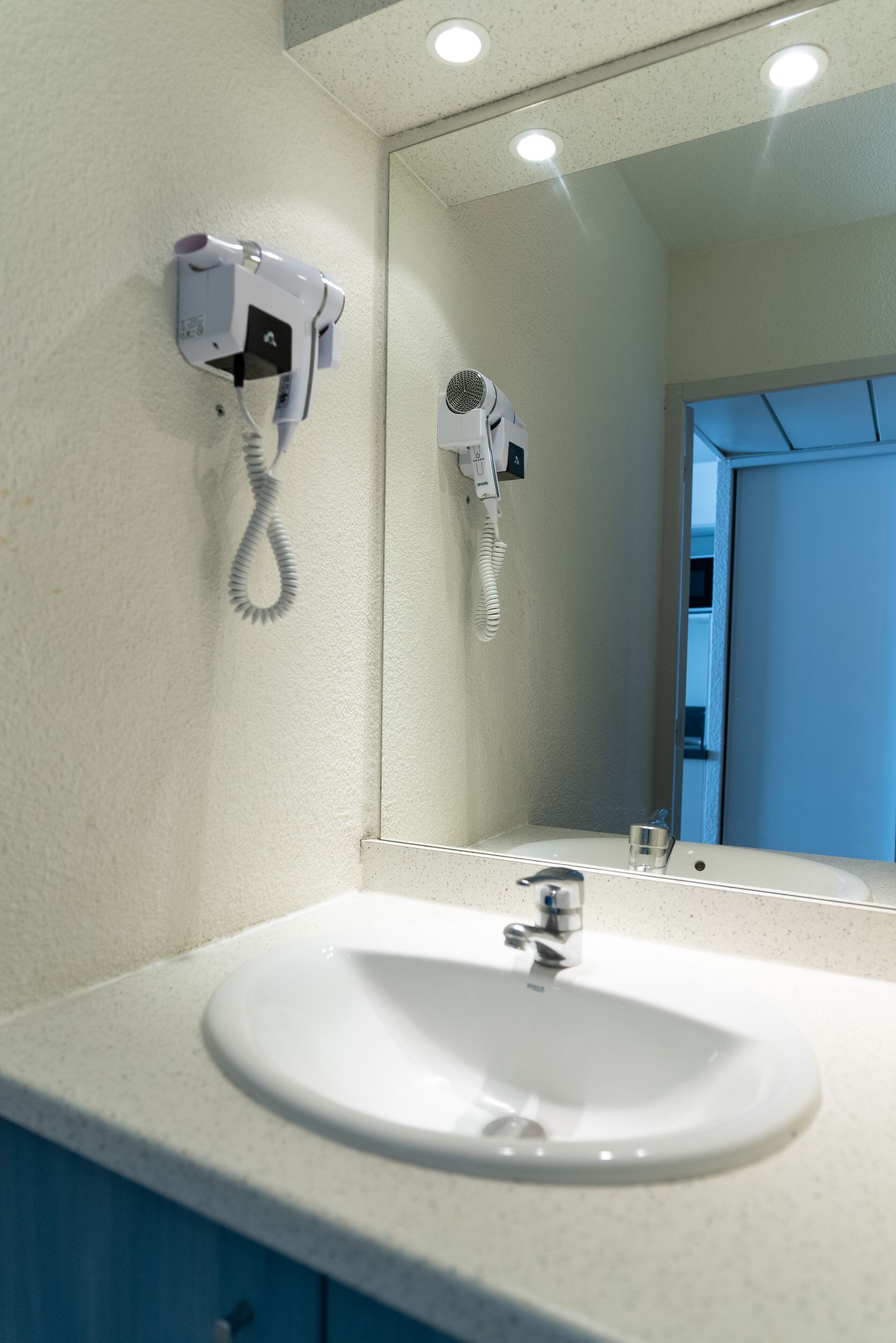A bathroom with a white sink, a mirror, and two hair dryers mounted on the wall.