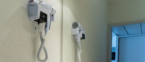 A bathroom with a white sink, a mirror, and two hair dryers mounted on the wall.