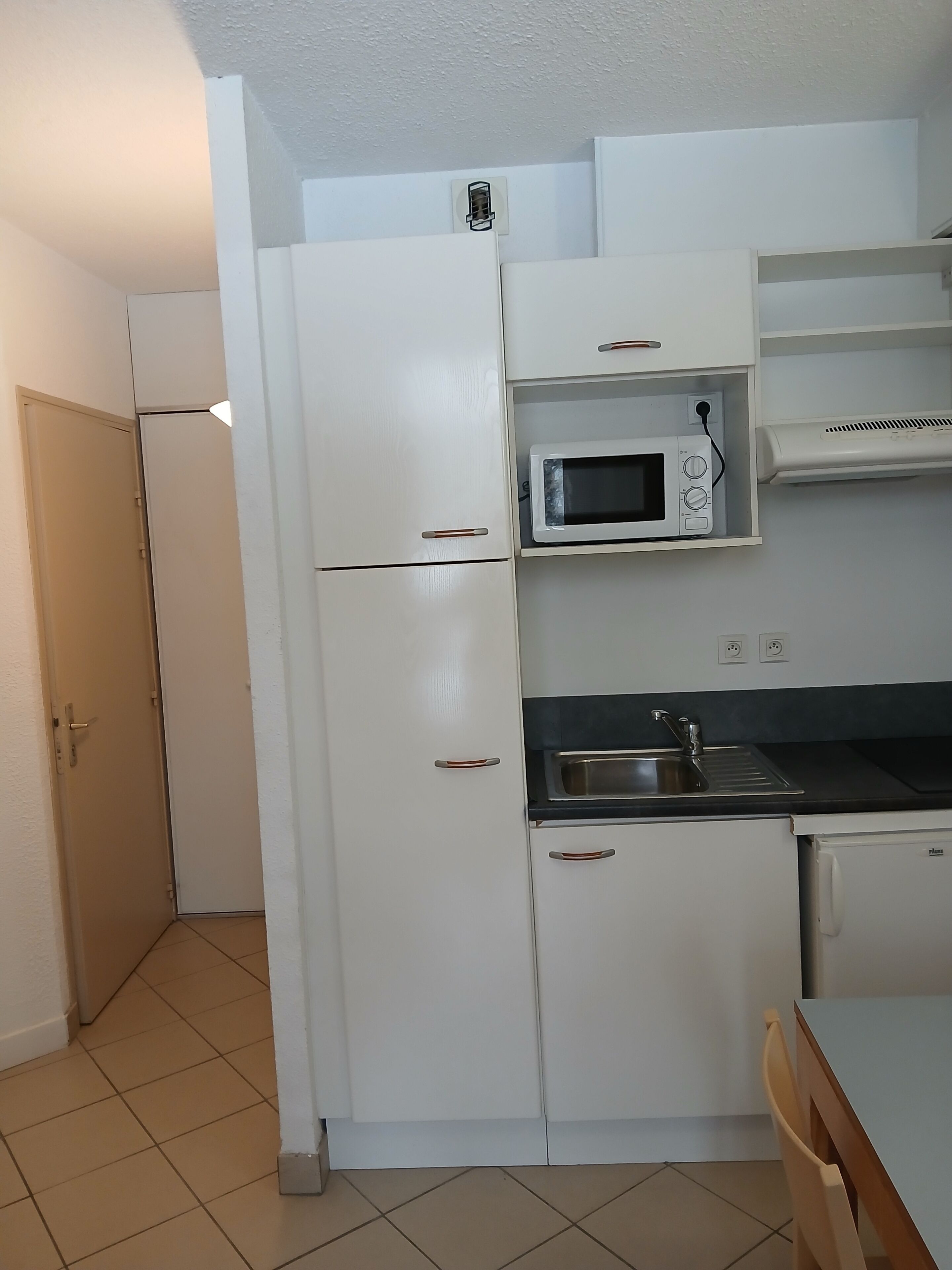 A compact kitchen with a refrigerator, microwave, sink, and a small countertop.