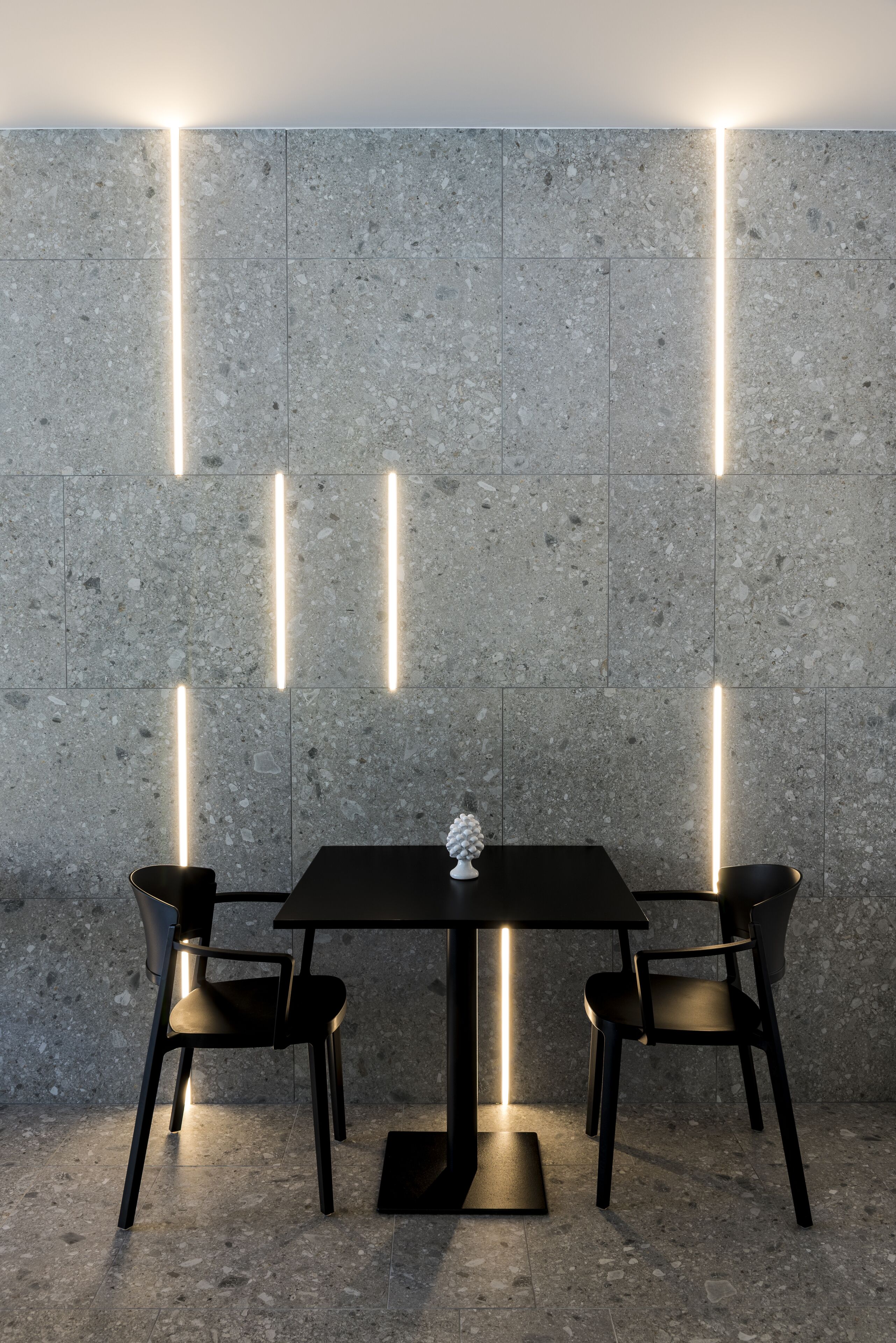 A modern dining area with a black table and chairs, illuminated by vertical light strips on the wall.