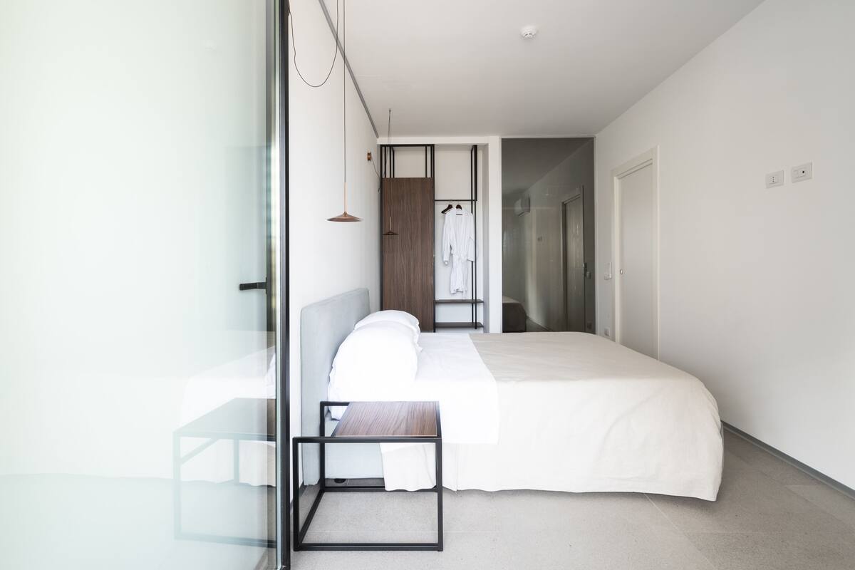 A modern bedroom with a large bed, a bedside table, a hanging light, and a view of a bathroom.