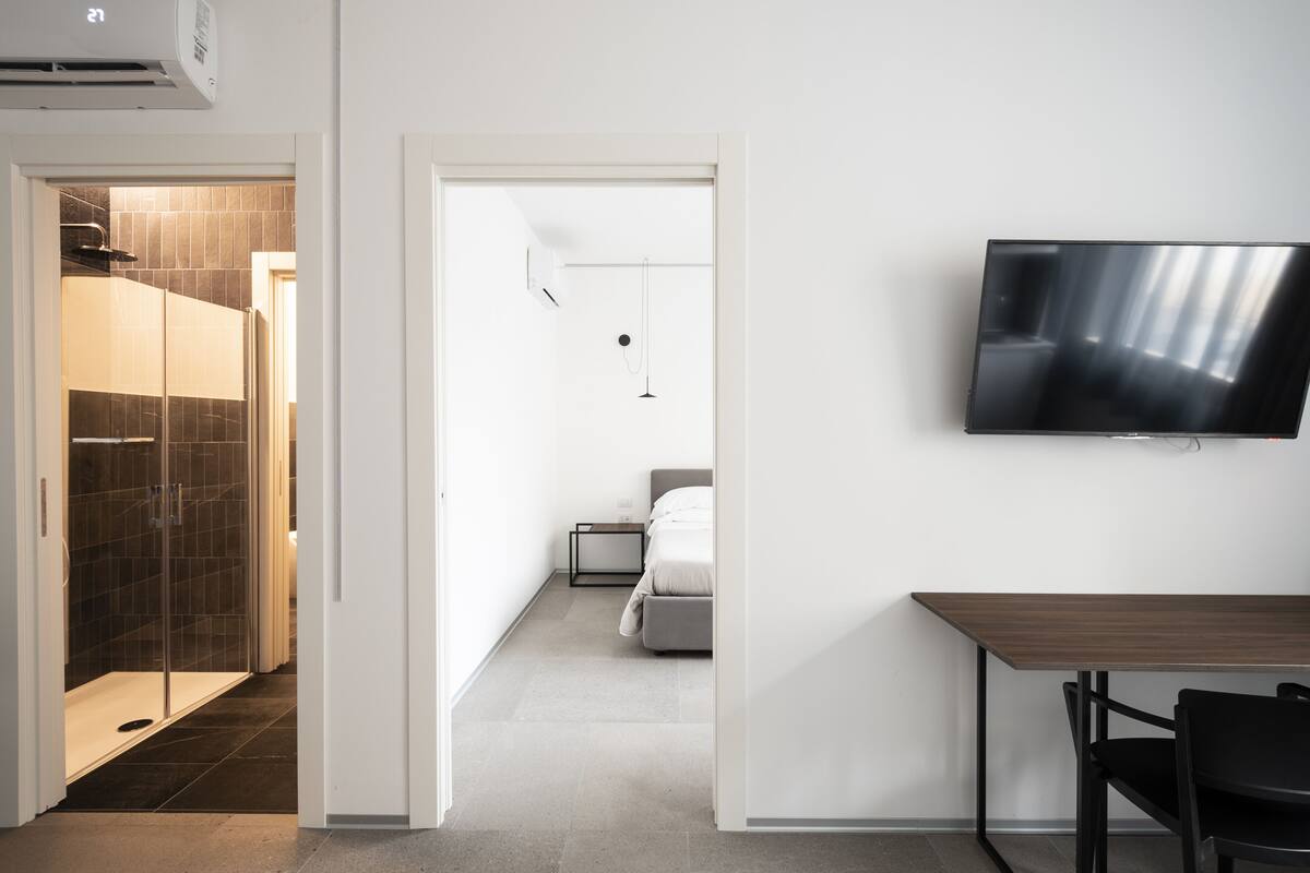 A modern hotel room with a shower, bed, bedside table, and a mounted TV.