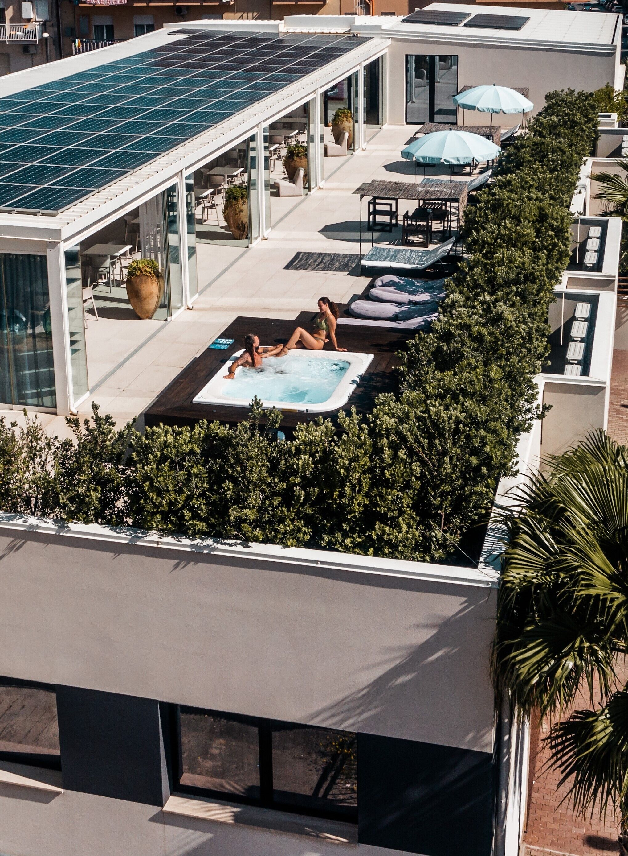 A rooftop pool area with solar panels, lounge chairs, and a hot tub.