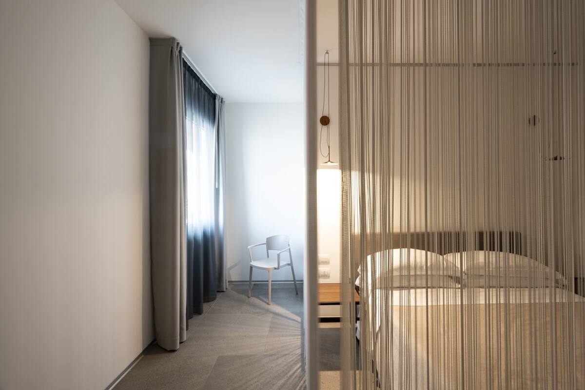 A modern hotel room with a bed, a chair, and a curtain.
