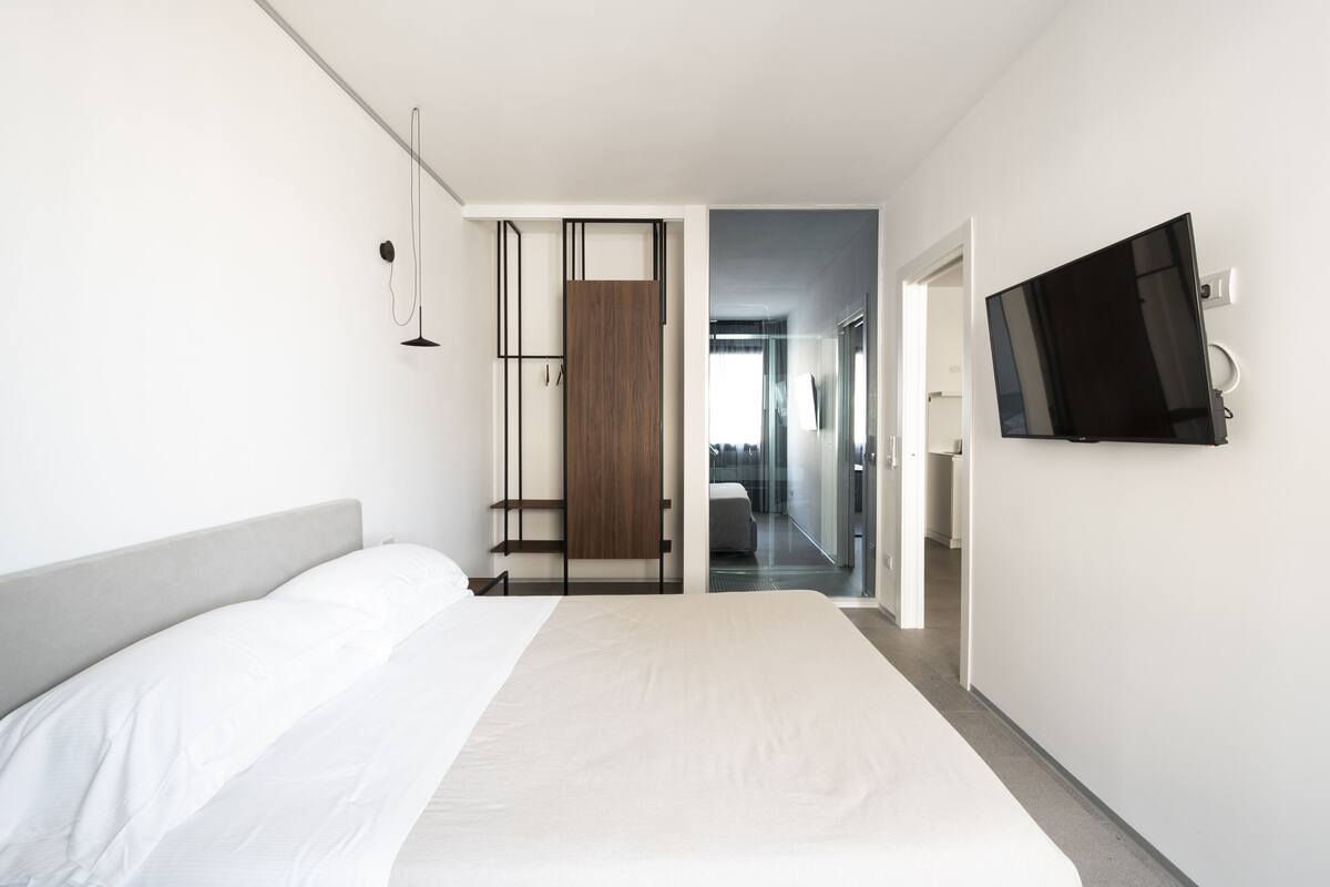 A modern hotel room with a large bed, a TV mounted on the wall, and a walk-in closet.