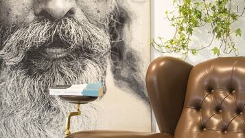 Un sillón de cuero marrón con respaldo capitonado, ubicado frente a una pared con un retrato grande en blanco y negro y una planta colgante.