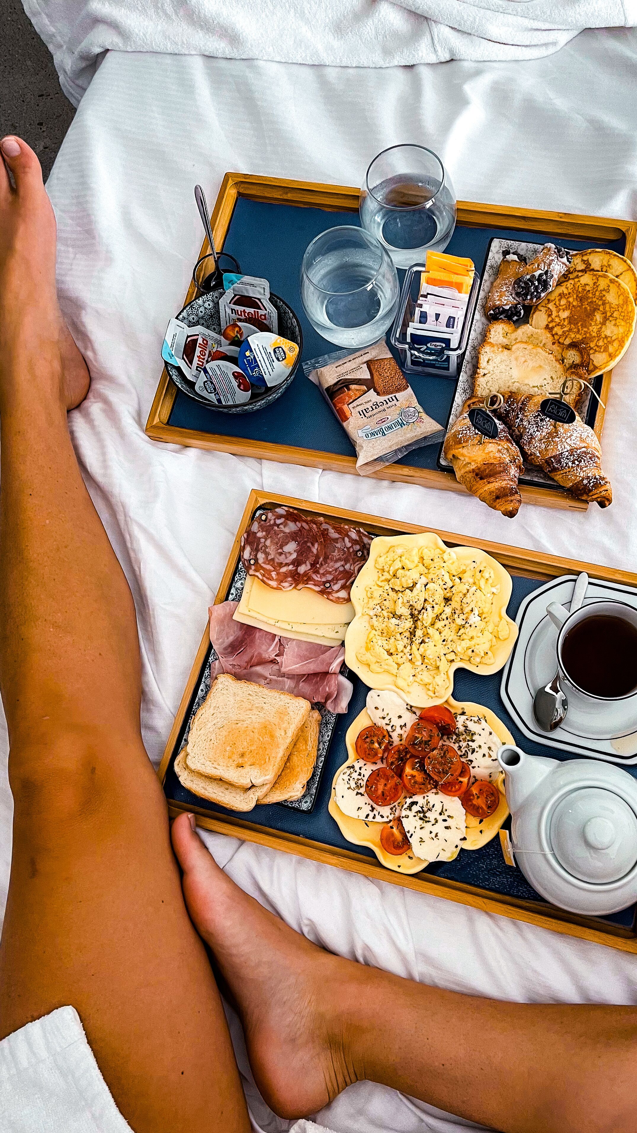 Un plateau de petit-déjeuner avec des croissants, des viennoiseries, du fromage et une tasse de café, posé sur un lit.