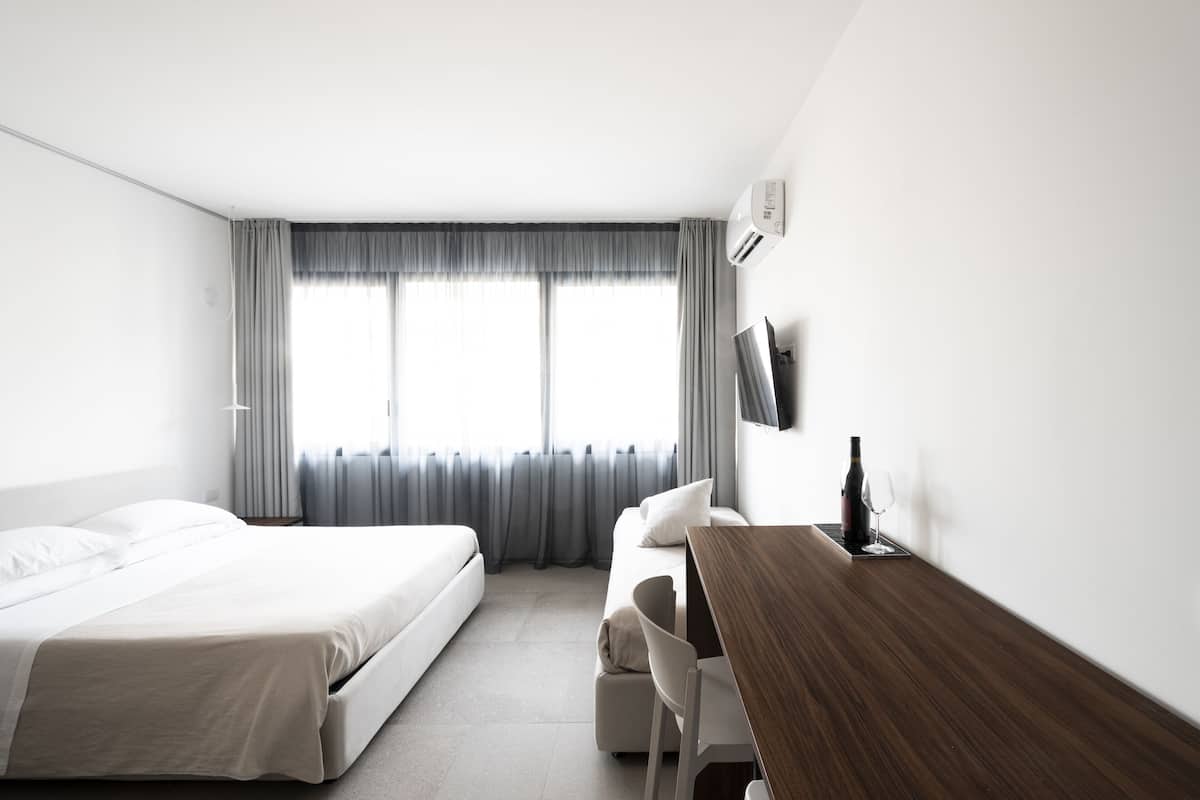 A modern hotel room with a bed, a desk, a chair, and a TV.