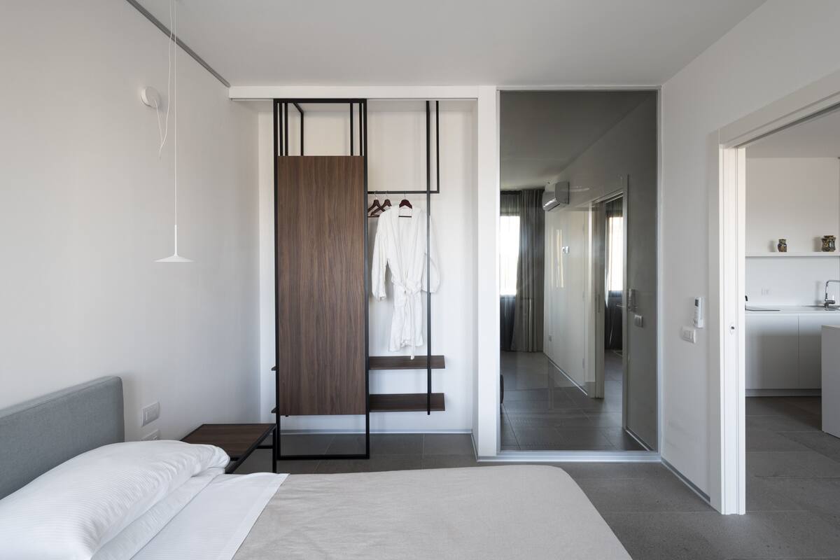 A modern hotel room with a bed, a wardrobe, and a bathroom visible through an open door.