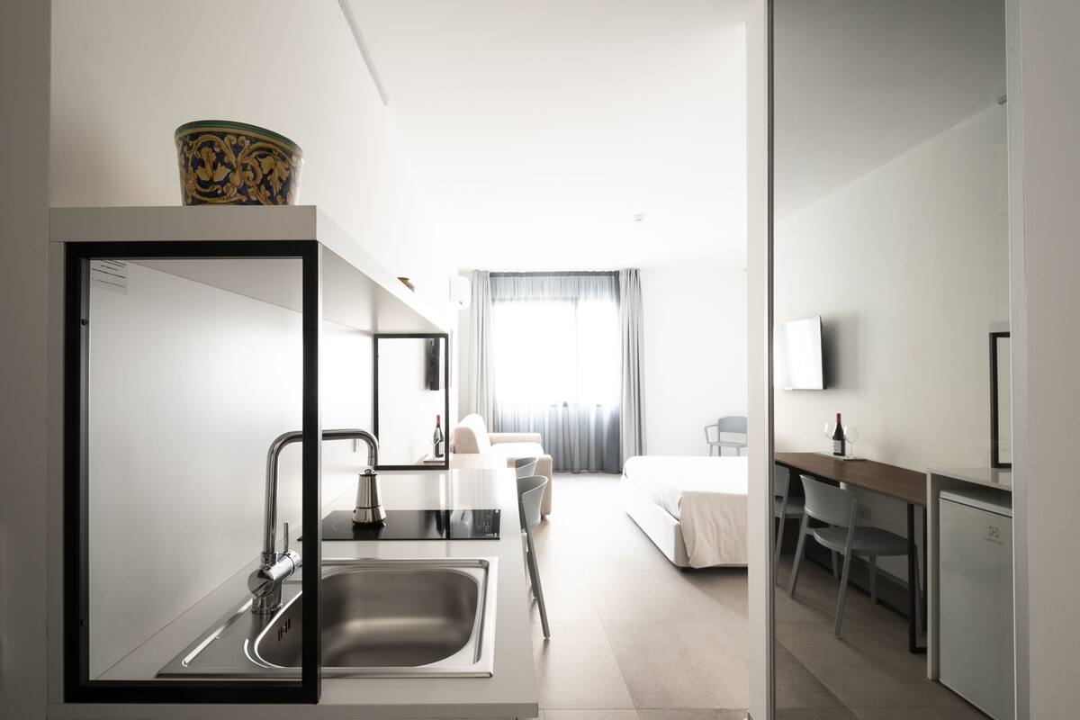 A modern hotel room with a bathroom, a bed, a desk, and a TV.