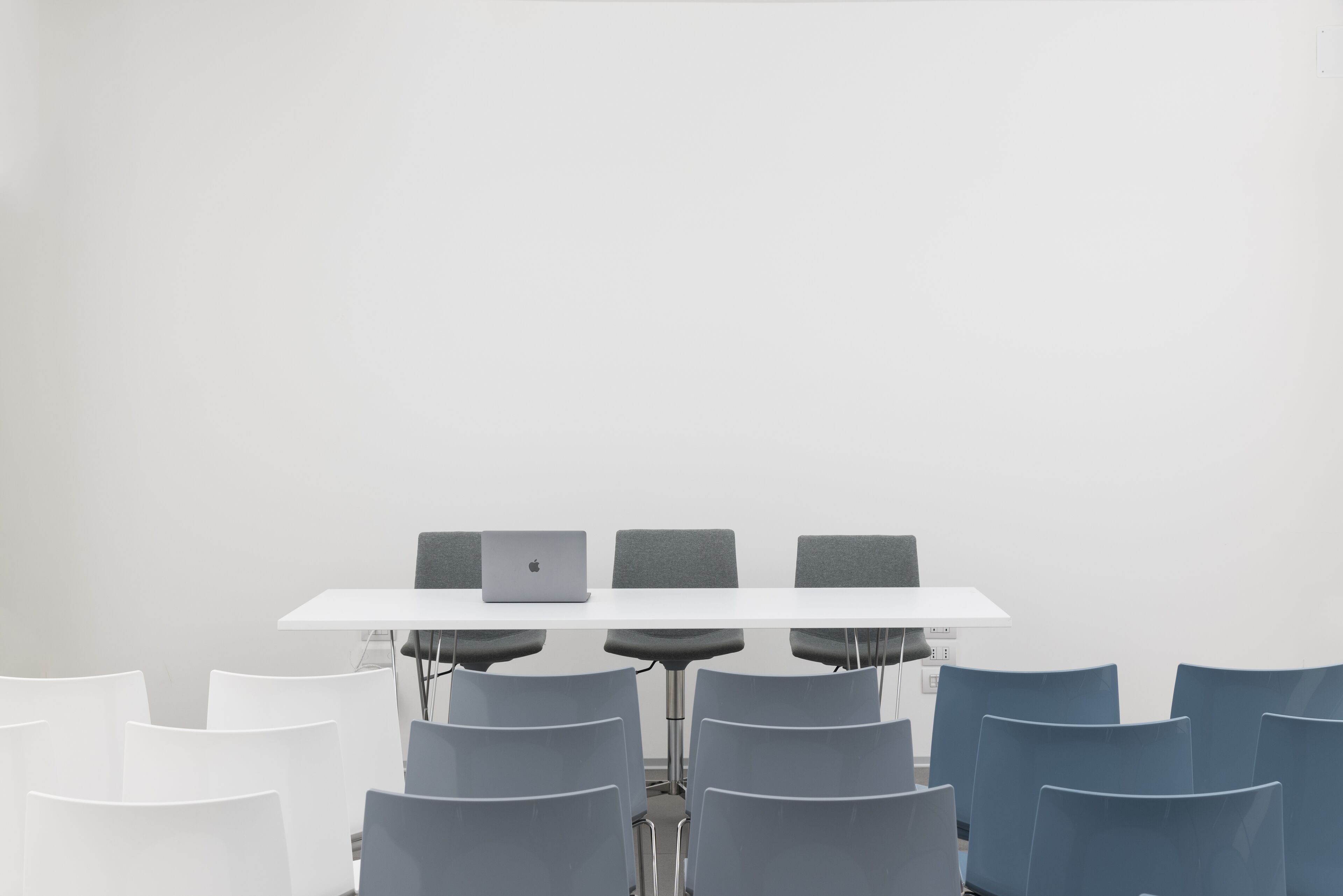 A conference room with a white table, grey chairs, and a laptop on the table.