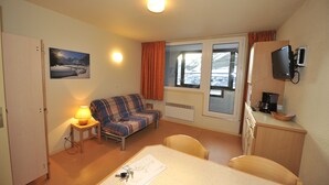 Une chambre d’hôtel de taille réduite, comprenant un lit, une petite table avec une chaise, un canapé, un téléviseur et une fenêtre avec des rideaux.