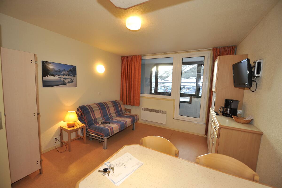Habitación de hotel compacta con cama, una mesita con una silla, un sofá, televisor y ventana con cortinas.