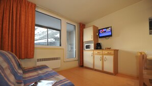 Une chambre d’hôtel de taille réduite, comprenant un lit, une kitchenette, un téléviseur et une fenêtre avec des rideaux.