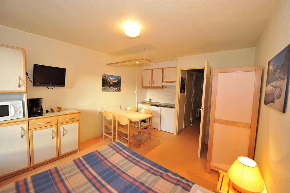 Cocina compacta con comedor, microondas, cafetera y televisor montado en la pared.