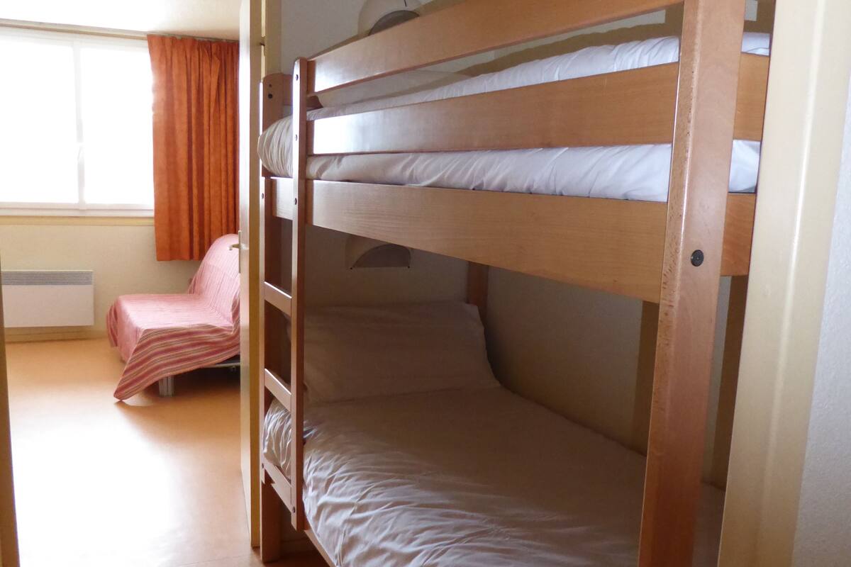 Habitación con literas, ventana, silla y radiador.