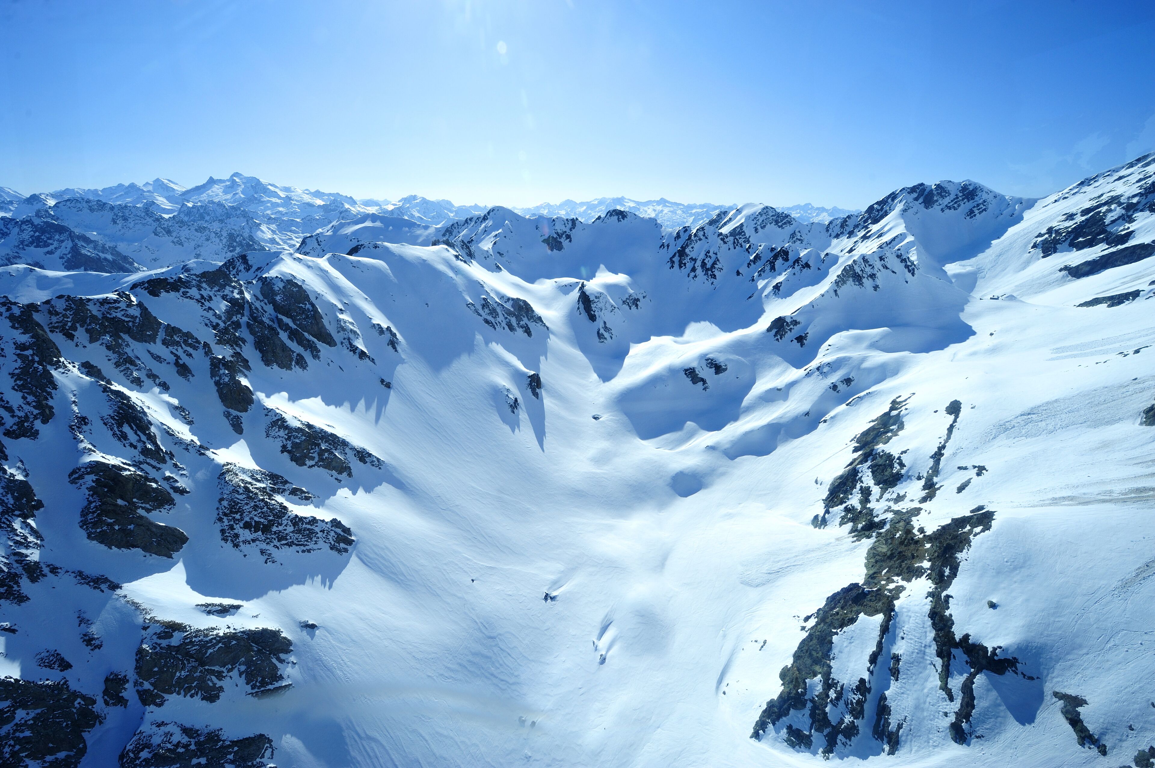 Un paisaje montañoso cubierto de nieve, con terreno accidentado y cielos despejados.