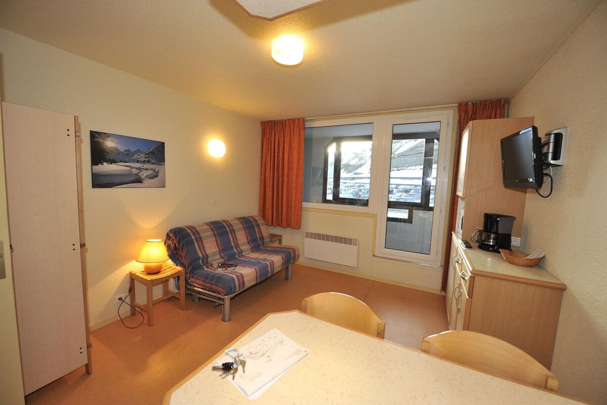 Una habitación acogedora con una cama, una mesita, un sofá, un televisor y una ventana con vistas a coches aparcados.