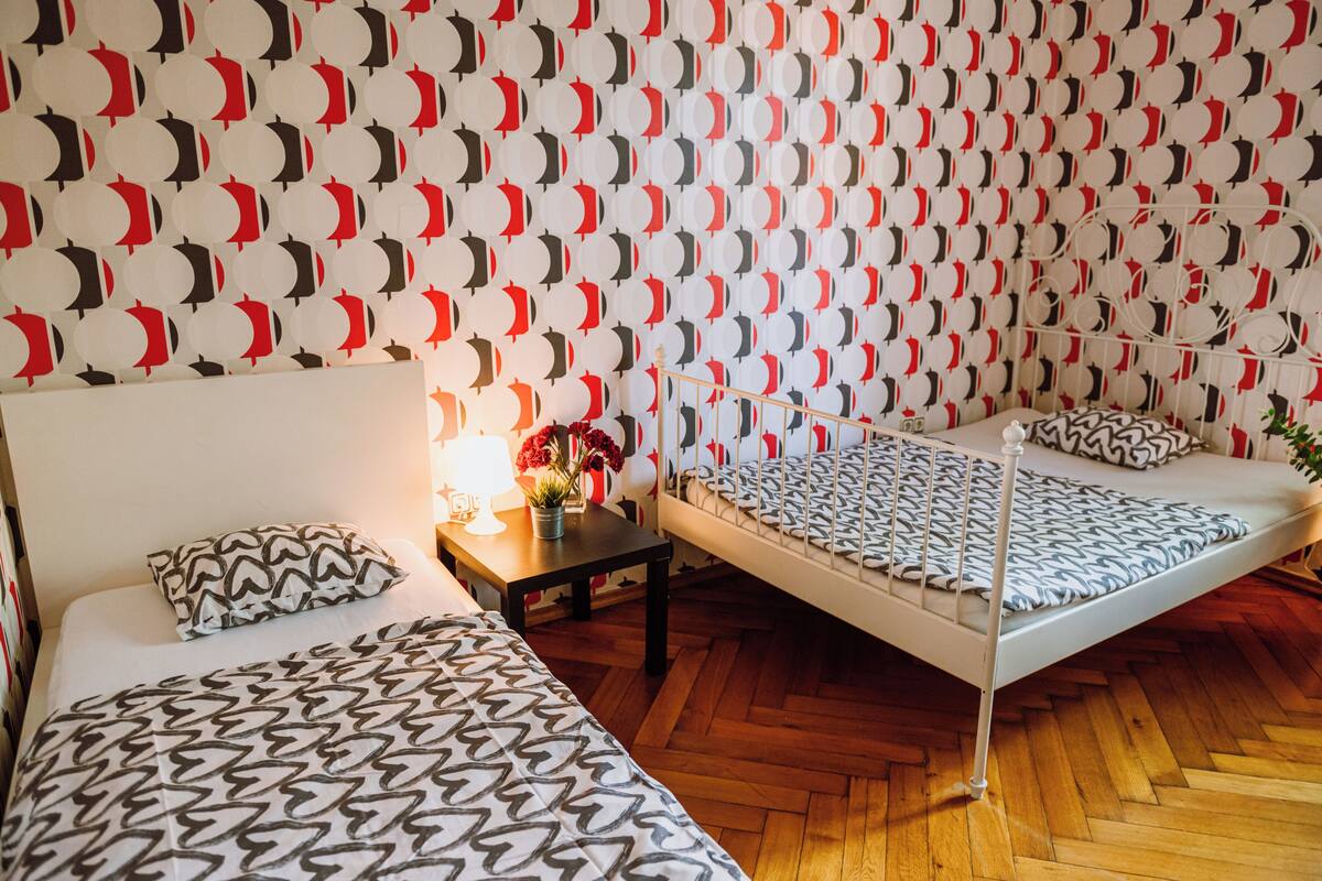 Una habitación con dos camas, una mesita de noche con lámpara y una pared con diseño.