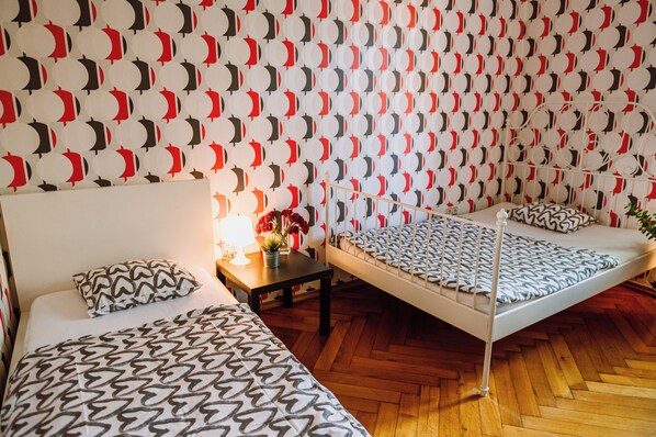 Una habitación con dos camas, una mesita de noche con lámpara y una pared con diseño.