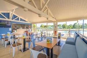 Un restaurant doté d’une terrasse, d’un bar et de grandes fenêtres donnant sur une piscine.