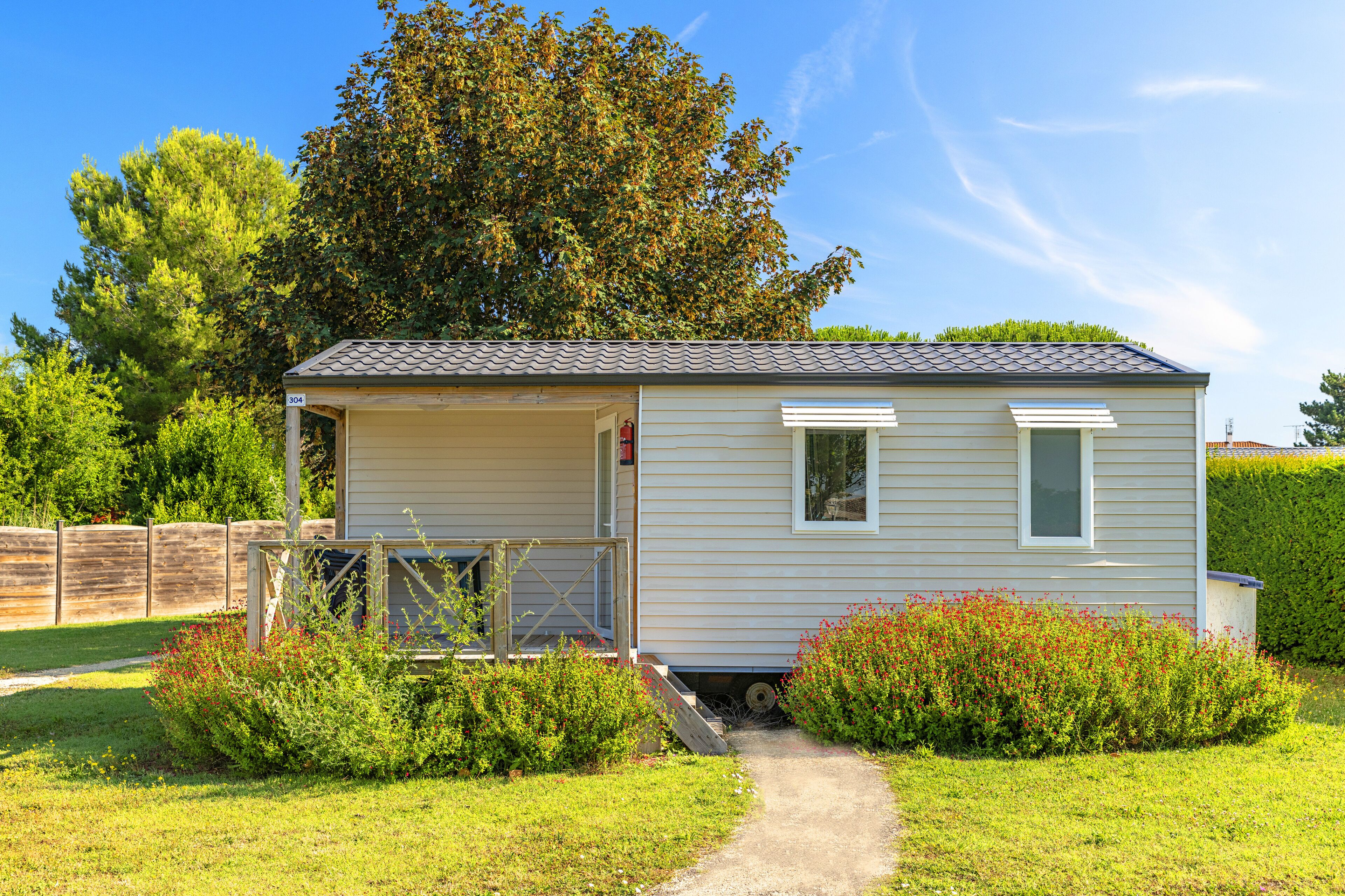 A small, single-story mobile home with a covered porch, a small window, and a pathway leading to the entrance.