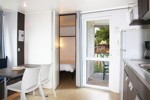 Une pièce compacte comprenant un lit, une table à manger avec des chaises, un coin cuisine et une porte-fenêtre coulissante donnant sur une terrasse extérieure.