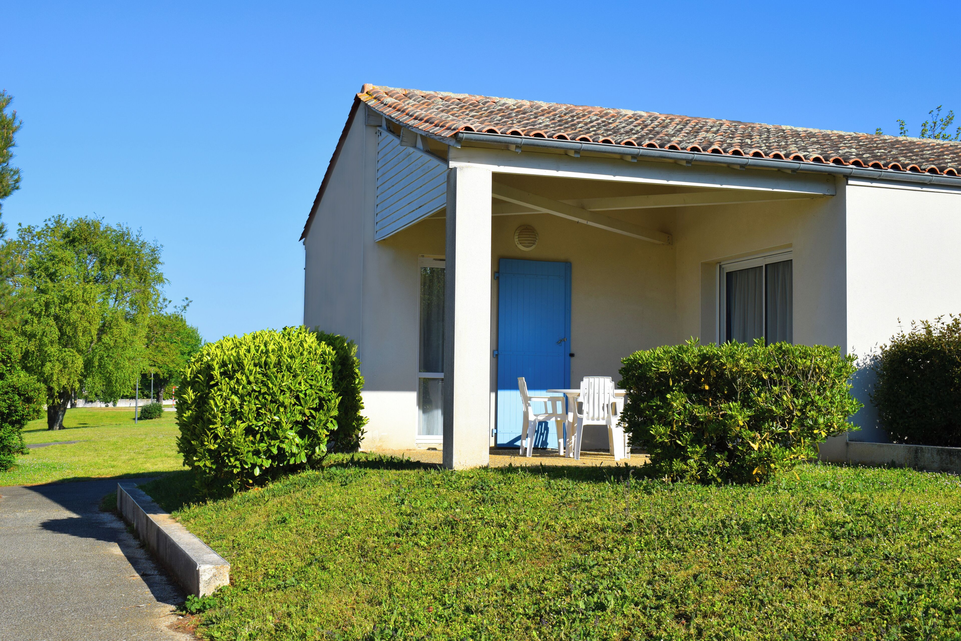 A single-story building with a tiled roof, a blue door, and a covered porch with outdoor seating.