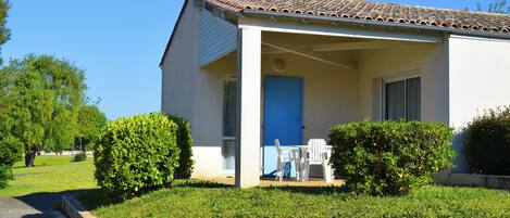 A single-story building with a tiled roof, a blue door, and a covered porch with outdoor seating.