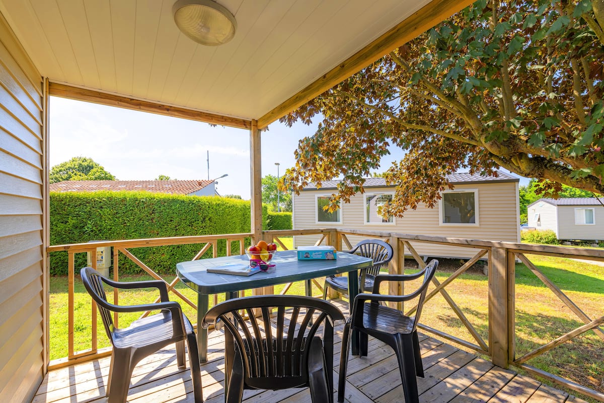 A covered outdoor area with a table and chairs, a fruit bowl, and a view of neighboring houses.