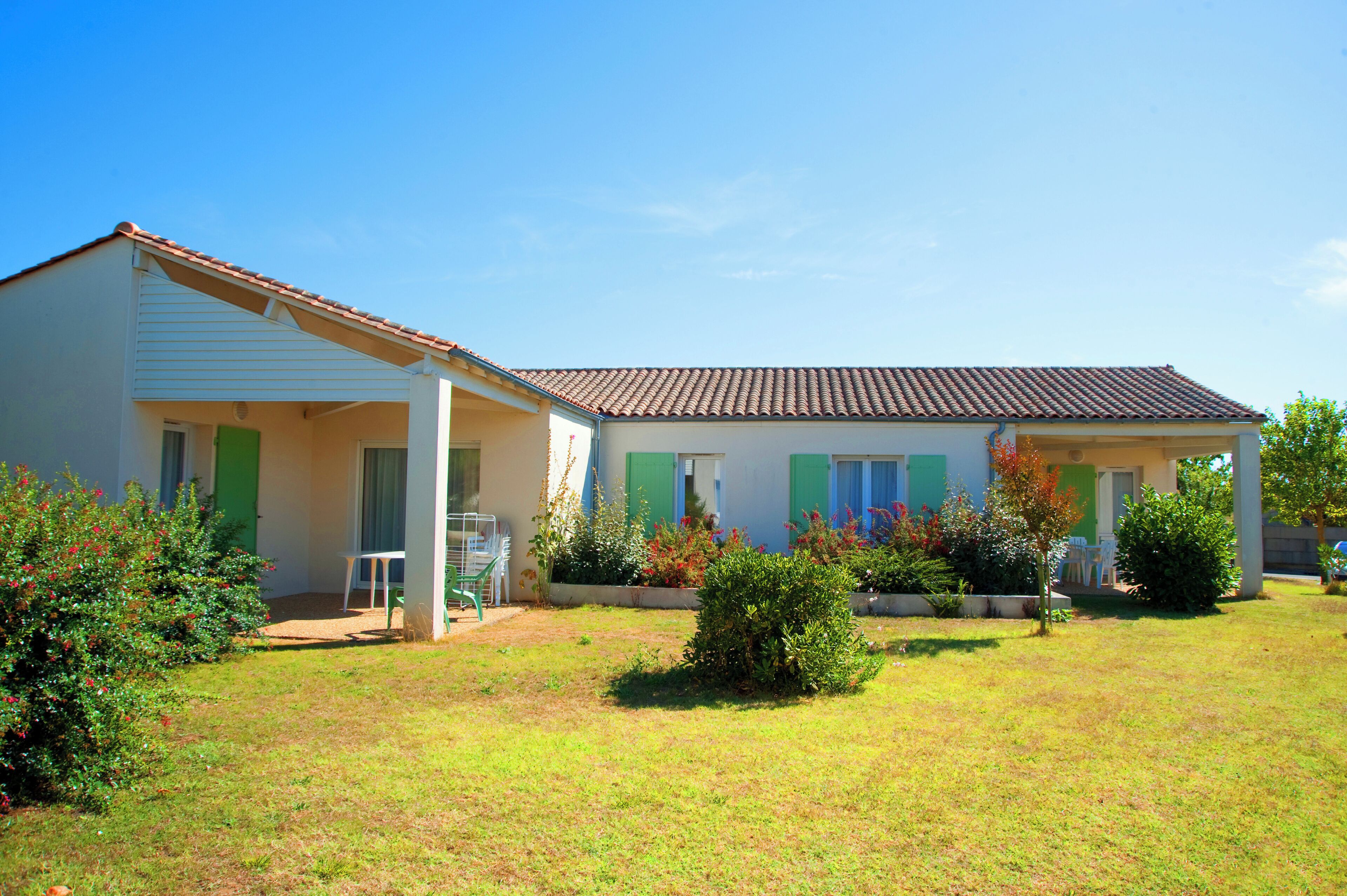A two-story house with a covered porch, a small garden, and a clear blue sky.