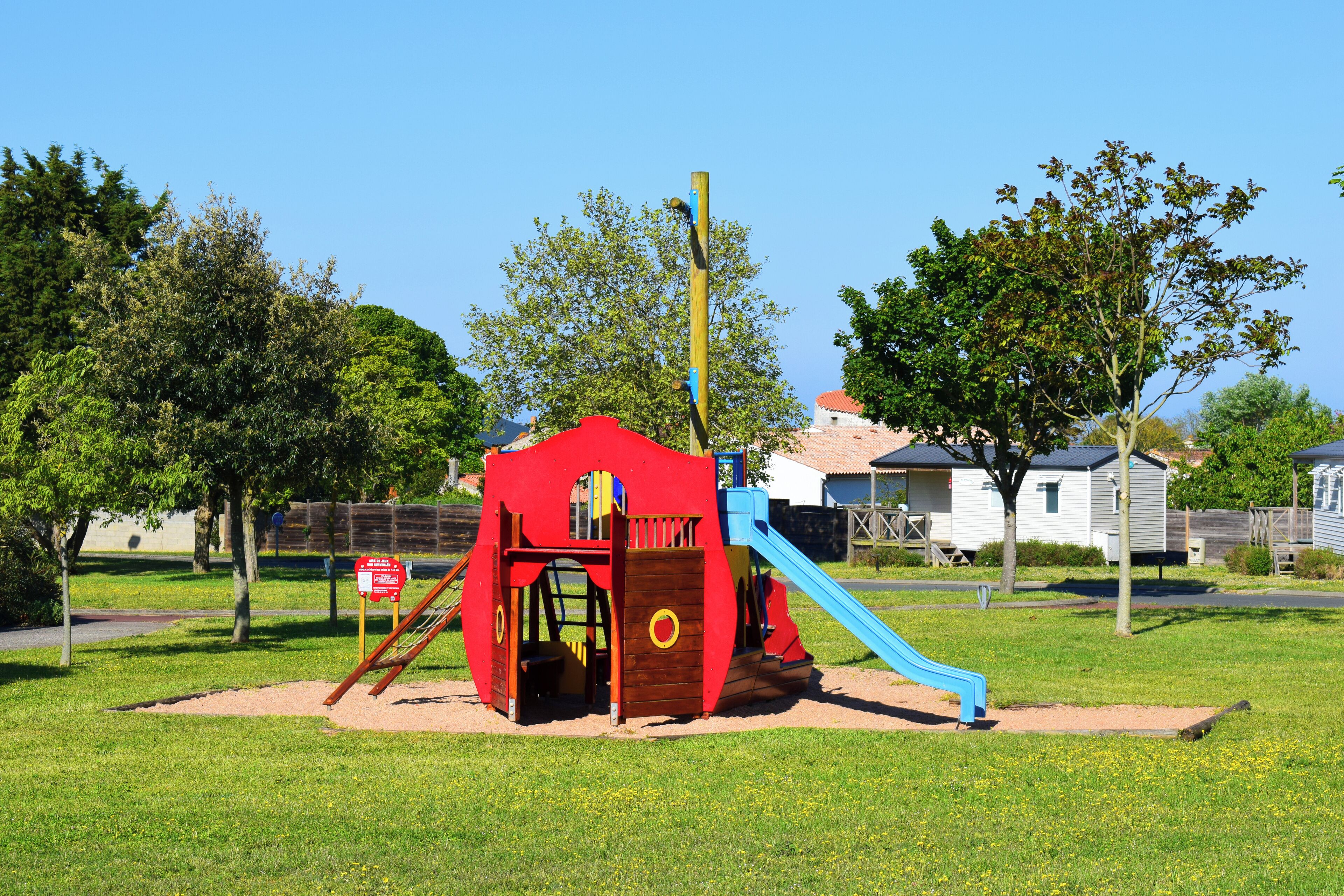 A playground with a red play structure and a blue slide.