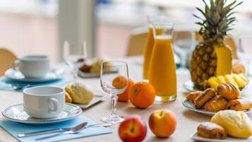 A breakfast table with a cup, glass, pineapple, oranges, and pastries.