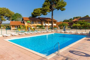 A swimming pool with lounge chairs, a children's play area, and a building with a tiled roof. - Azureva La Londe Les Maures (La Londe-les-Maures)