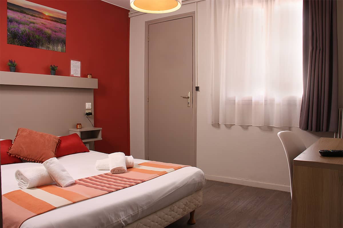 Ein Hotelzimmer mit Bett, Schreibtisch, Stuhl, Tür und einem Fenster mit Vorhängen.