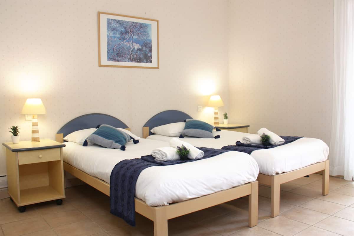Ein Doppelbett mit zwei Nachttischen, an jedem Tisch eine Lampe, eine kleine Pflanze und ein gefaltetes Handtuch. Darüber an der Wand hängt ein gerahmtes Bild.
