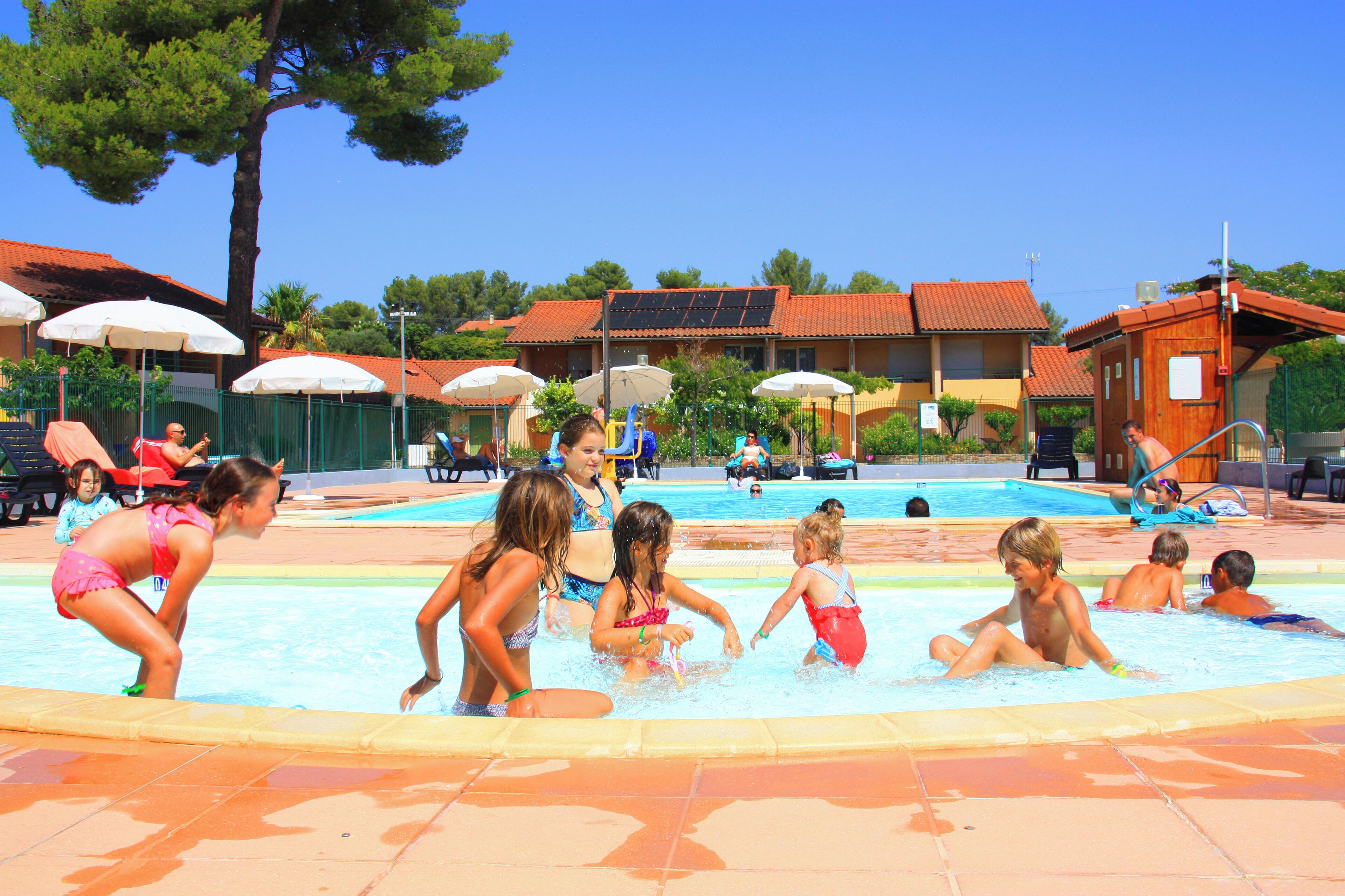 Un espace piscine comprenant plusieurs bassins, des parasols et des personnes.