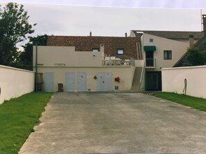 A building with a concrete driveway leading to a set of doors, a small balcony, and a window. - Hotel De La Mare (Avrigny)