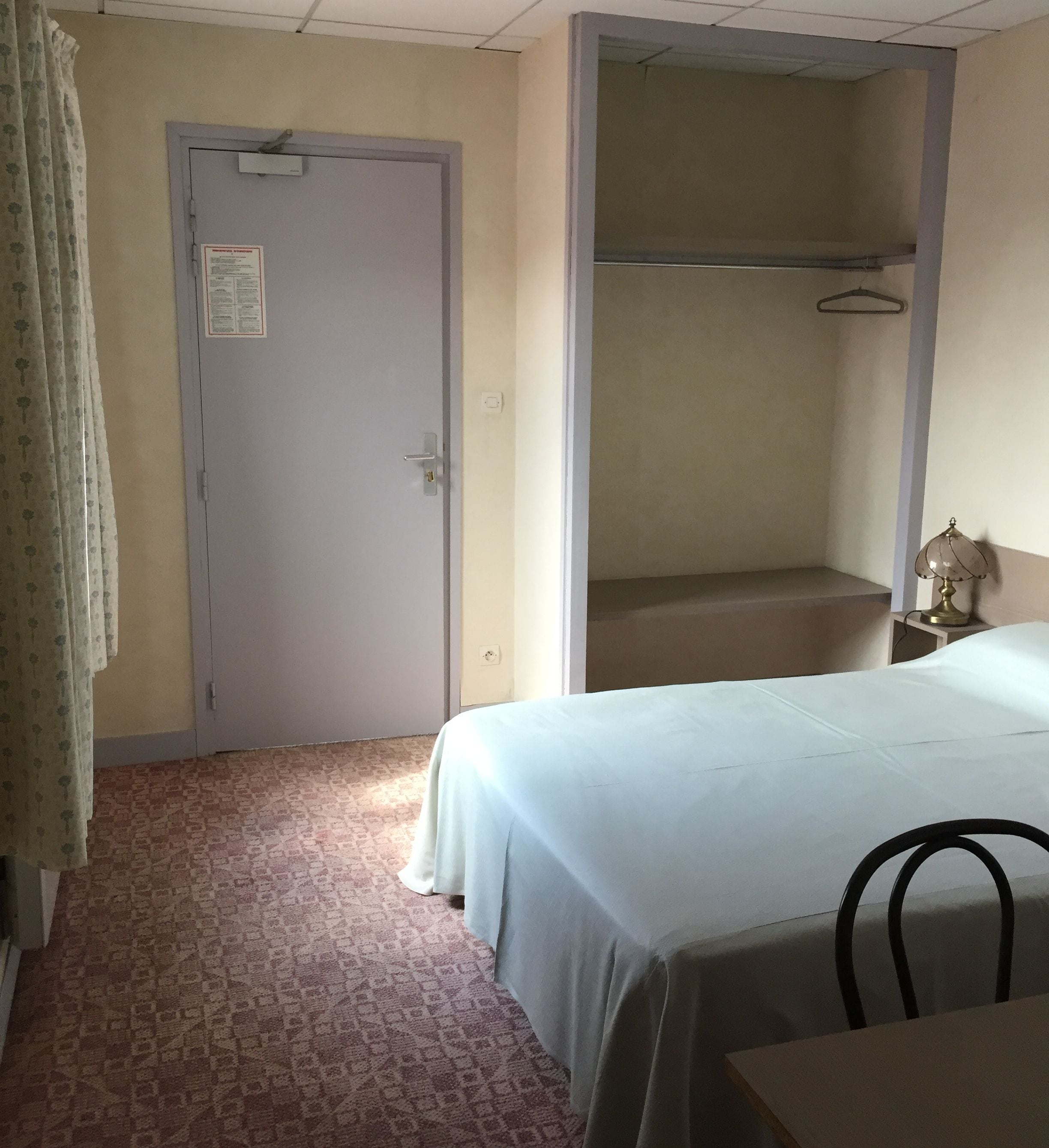 Une chambre d’hôtel avec un lit, une chaise, un bureau, une armoire et une porte.