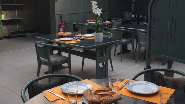 Un área de comedor al aire libre con mesas dispuestas para comidas, que incluye platos, cubiertos y pan.