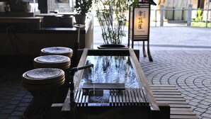A traditional Japanese water feature with a wooden bench in the foreground. - TOKIWAYA Ryokan (Nozawaonsen)