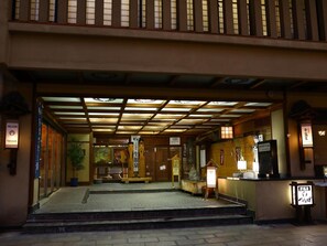 A traditional Japanese building entrance with a wooden structure, a tiled floor, and a sign welcoming visitors.