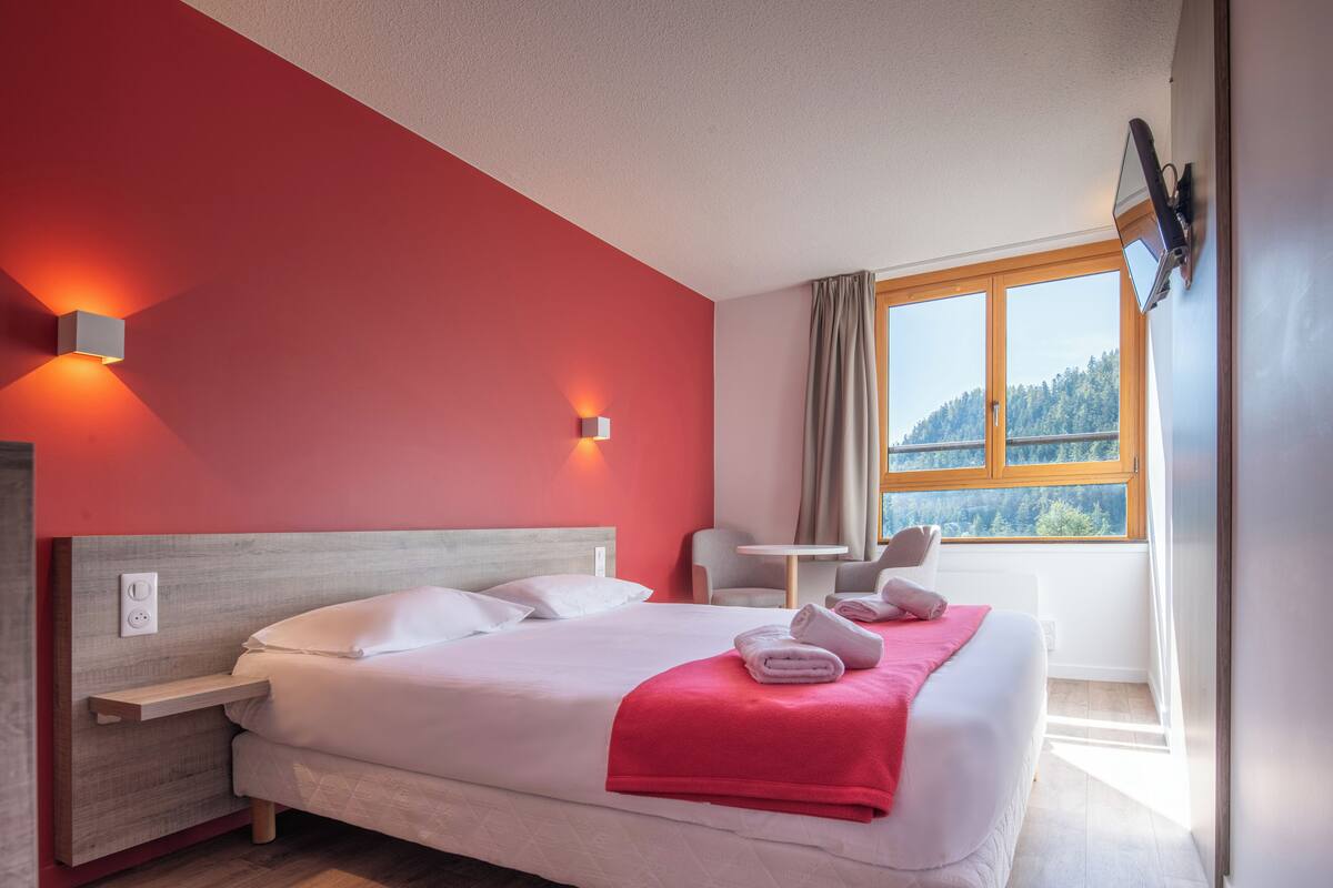 Una camera d'albergo con un letto, una scrivania, una sedia e un televisore fissato al muro.