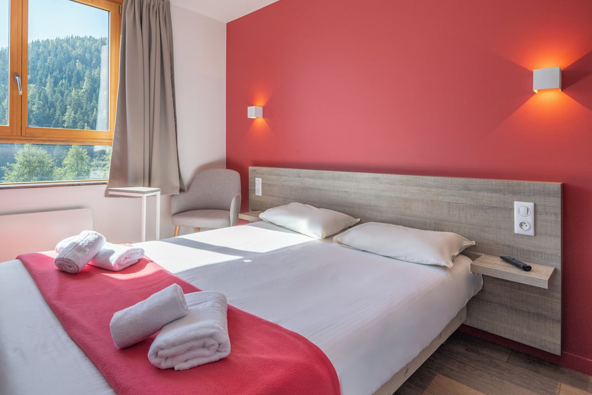 Camera d'albergo con un letto grande, una sedia, un comodino e una finestra con vista sugli alberi.