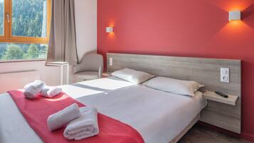 Ein Hotelzimmer mit einem großen Bett, einem Sessel, einem Nachttisch und einem Fenster mit Blick auf Bäume.
