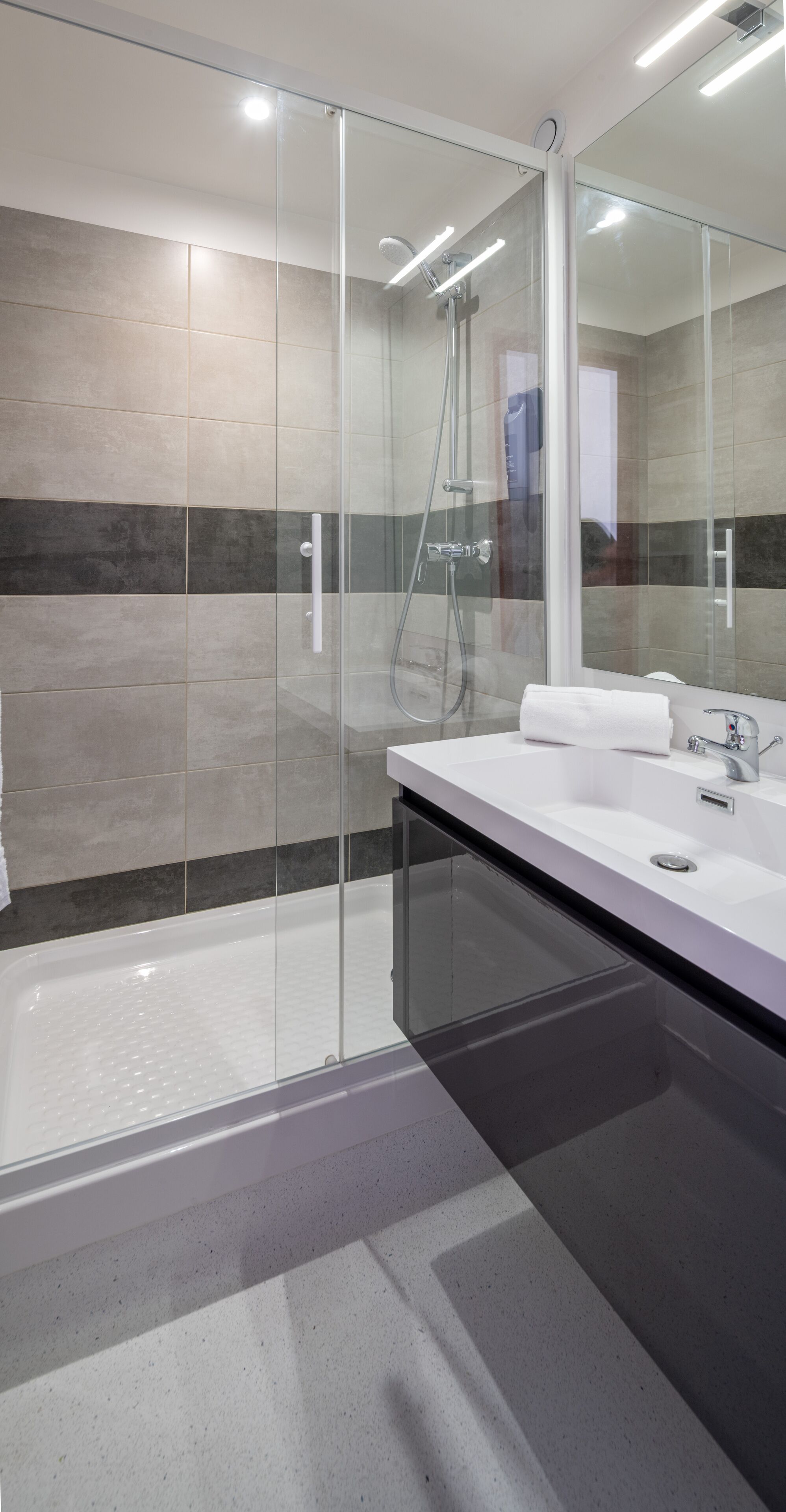 A modern bathroom with a glass-enclosed shower, a white sink, and a large mirror.