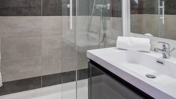A modern bathroom with a glass-enclosed shower, a white sink, and a large mirror.